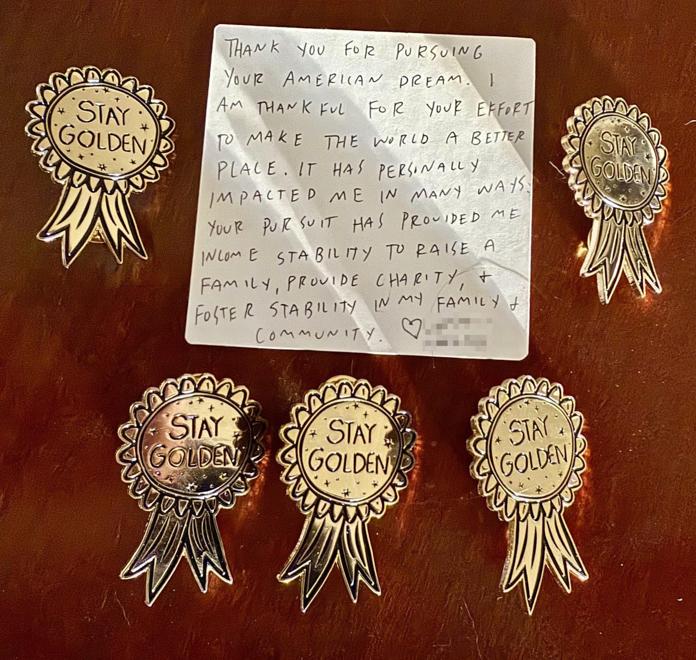 handwritten note: "Thank you for pursing your American Dream. I am thankful for your effort to make the world a better place. It has personally impacted me in many ways: your pursuit has provided me income stability to raise a family, provide charity, and foster stability in my family and community. ❤️" surrounded by five Stay Golden pins from Hanna Gumbo's online store.