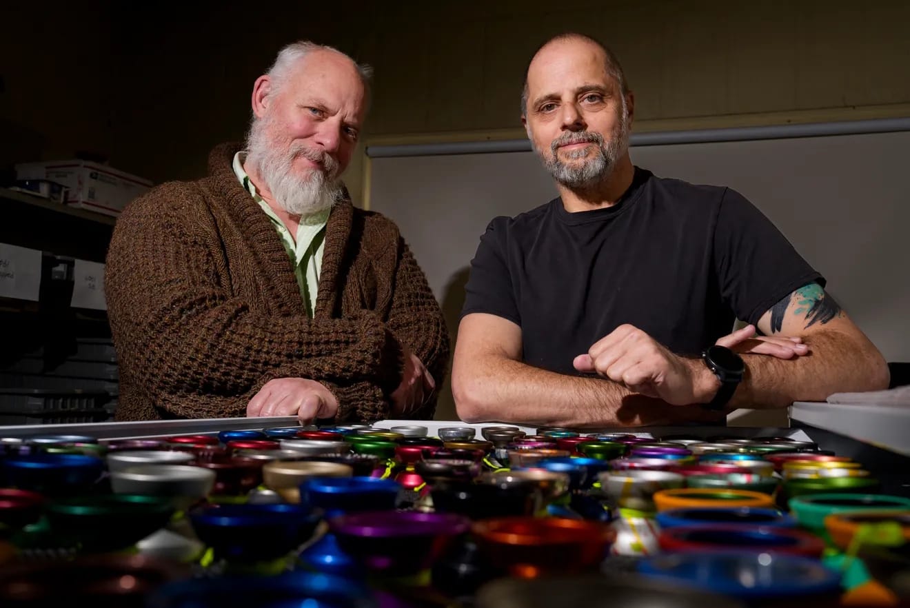 photo of David Metz and Shawn Nelson, at their machine shop in front of a large number of brightly colored yo-yos