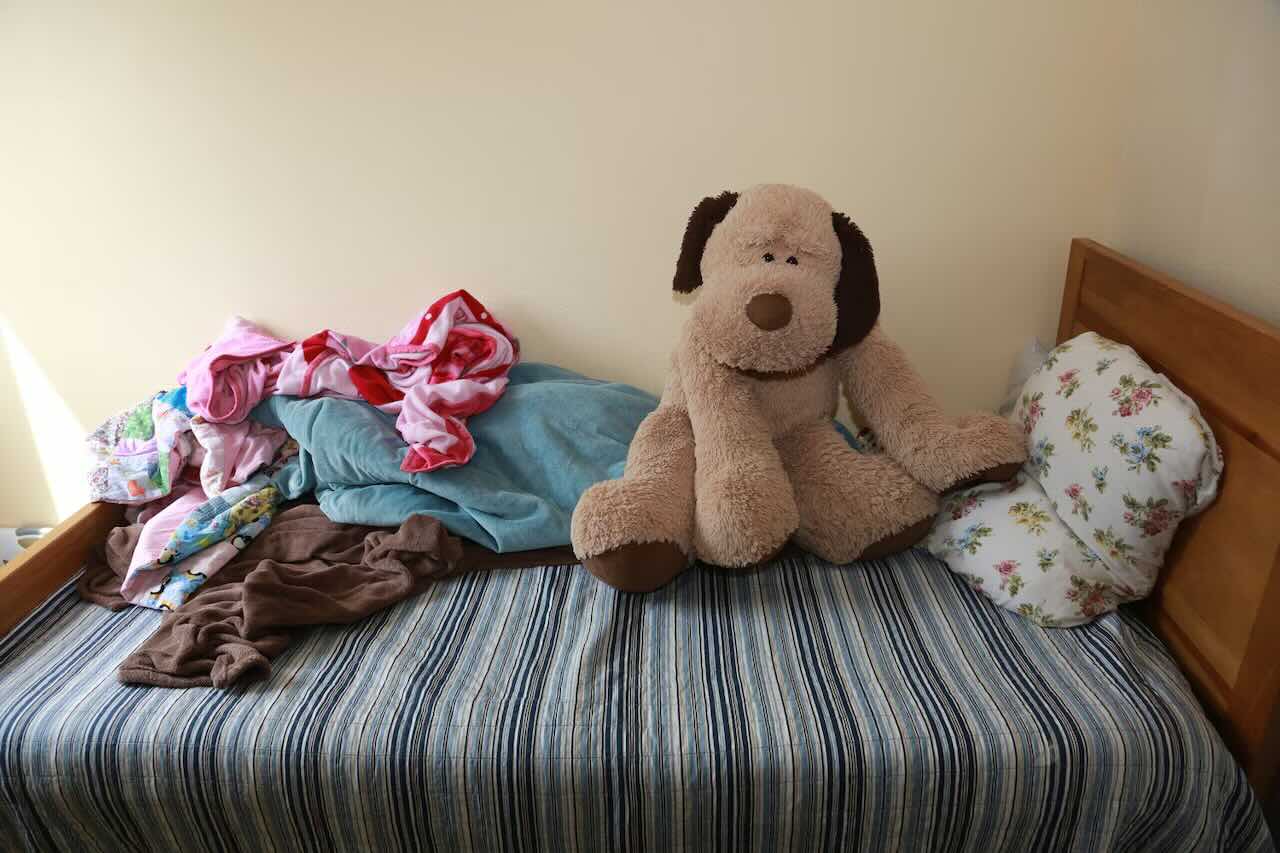 A photo of a bed, with clothes and a stuff dog on it. Ninety-four percent of homeless youth in a recent study found housing after being given a guaranteed income for two years.